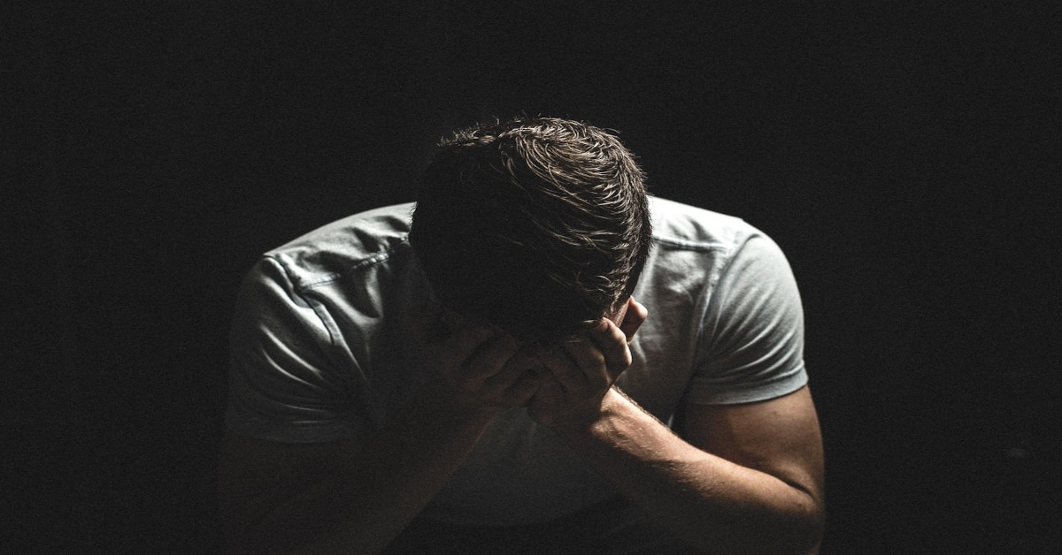 A man alone in the dark while holding his head.