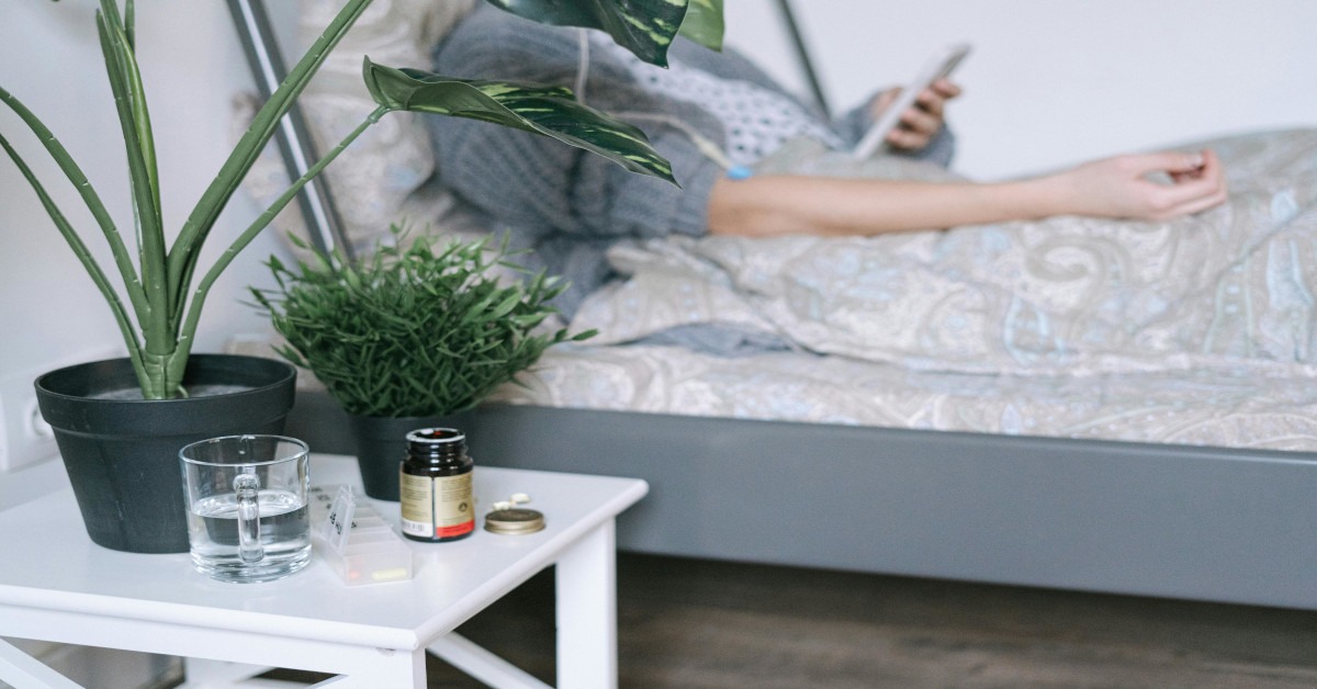 A sick woman lying in bed with and pills lying next to her.