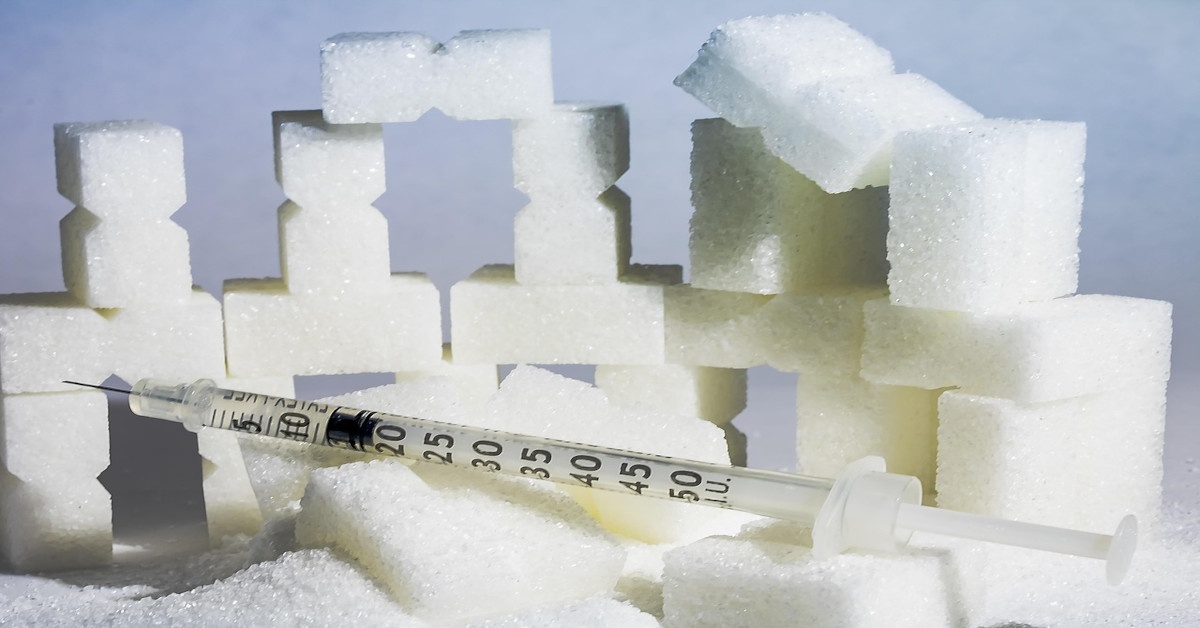 A syringe lying between cubs of sugar, indicating insulin resistance.