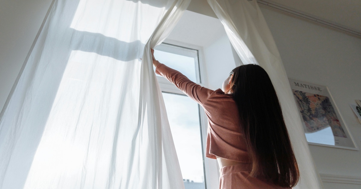 A woman opening a white curtain.