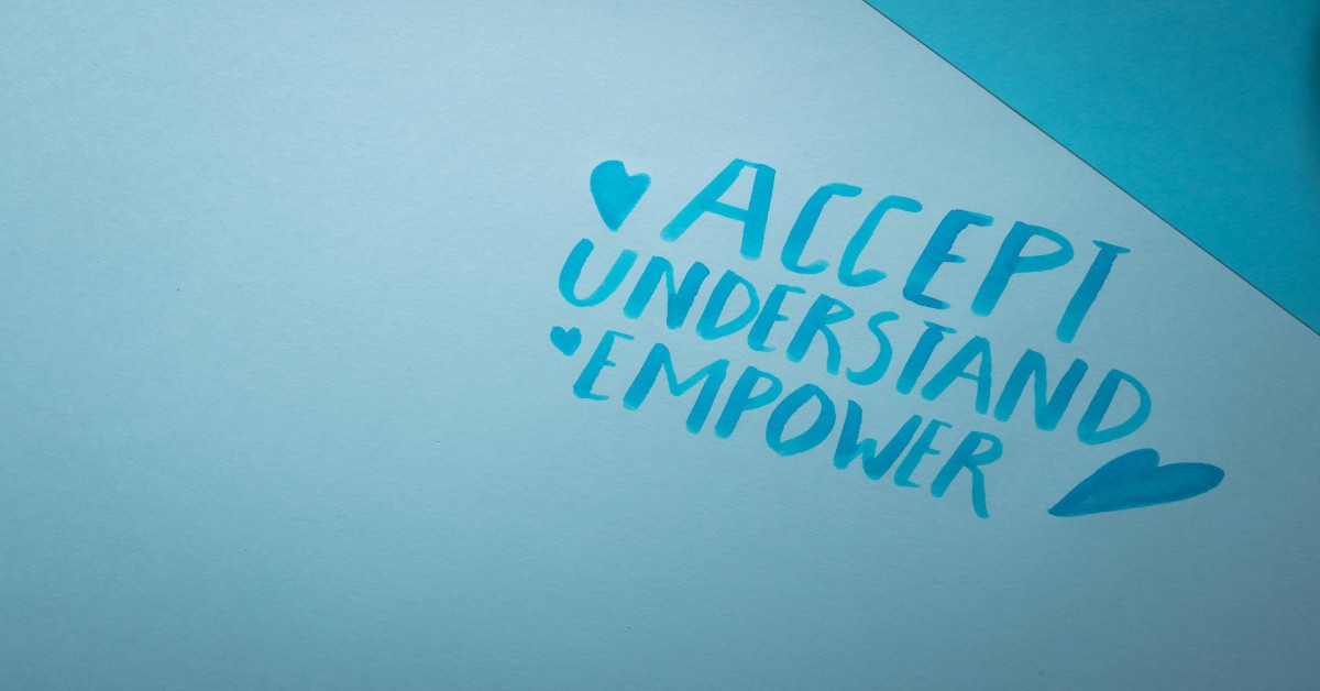 The words "accept, understand, and empower" written in blue ink on a blue background.