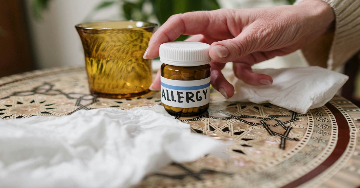 A person is grabbing a bottle of pills reading "allergy" with tissues lying around it.