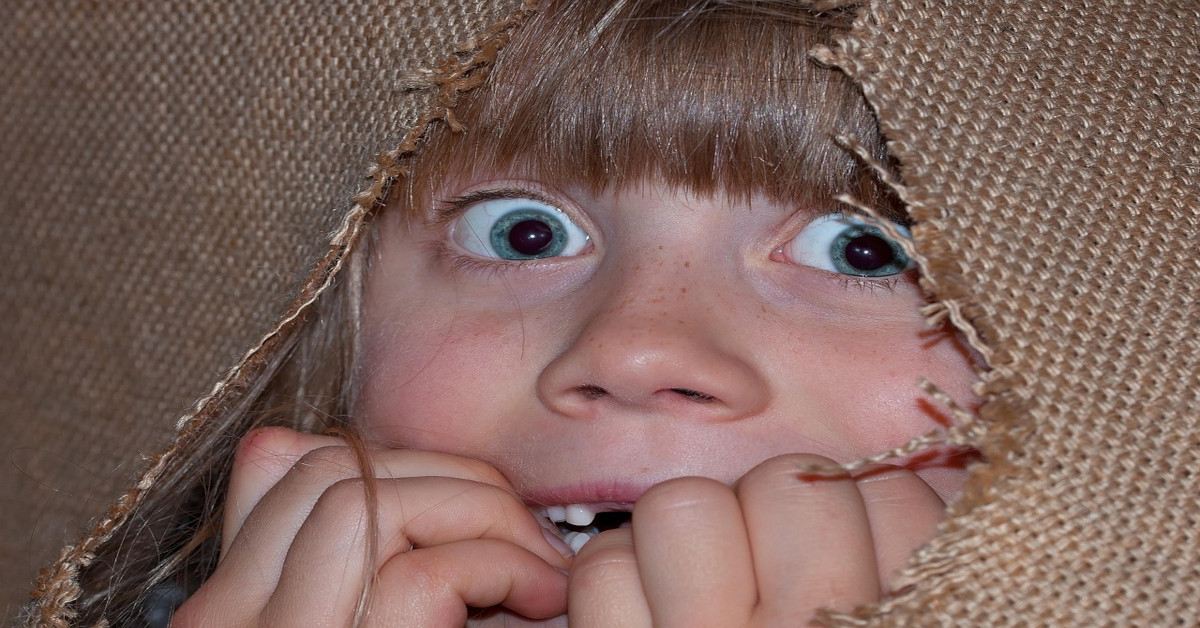A child looking anxious while holding her hands in front of her mouth.