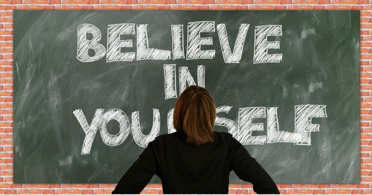 A woman looking at a blackboard that says "believe in yourself".