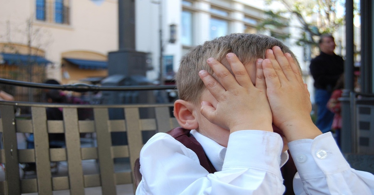 A little boy covering his face with his hands because he's feeling ashamed.