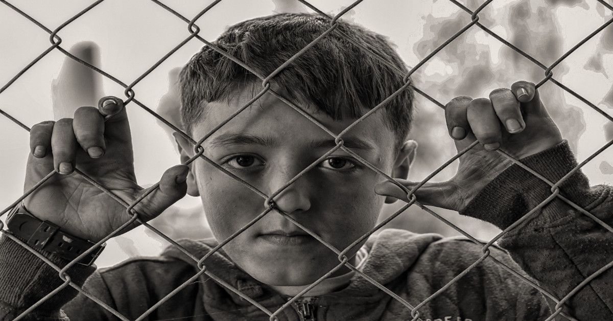 A young boy looking sad while grabbing a fence.