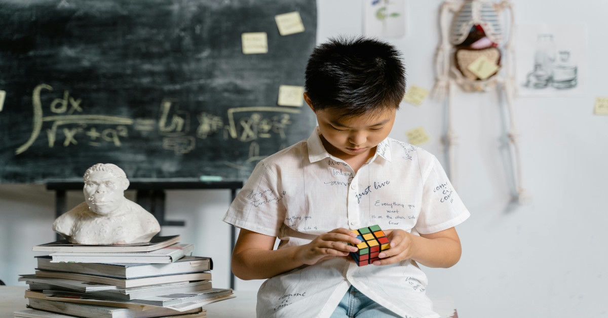 A boy solving a Rubik's Cube in a classroom.