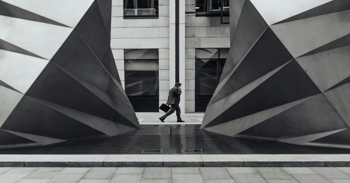 Black and white image of a businessman walking with a suitcase while calling on his cellphone.
