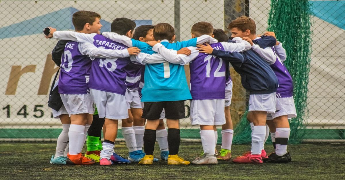 A team of children embracing each other while playing soccer.