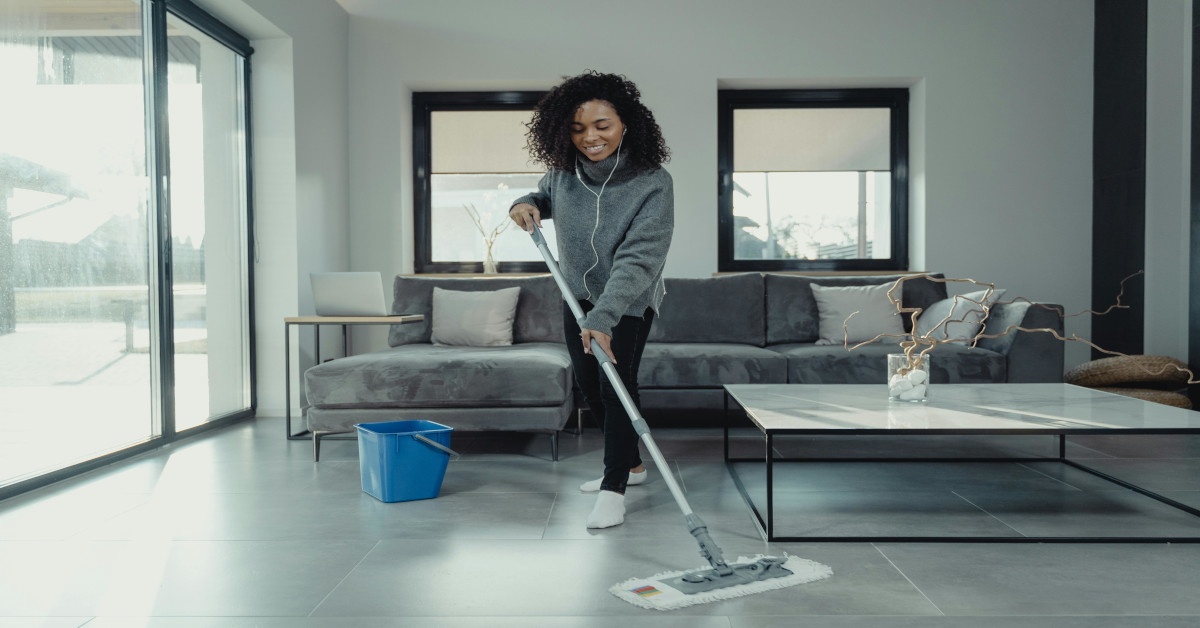 A dark skinned woman is cleaning with AirPods in.