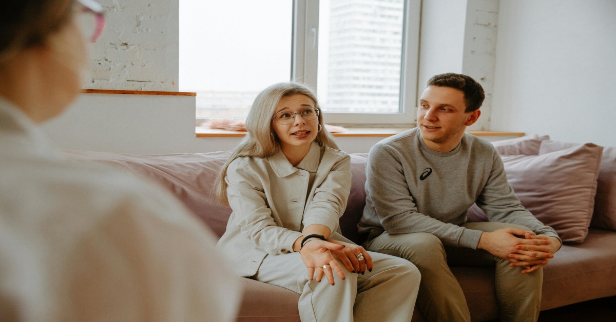 A couple going to relationship therapy and talking to a therapist while sitting on a couch.