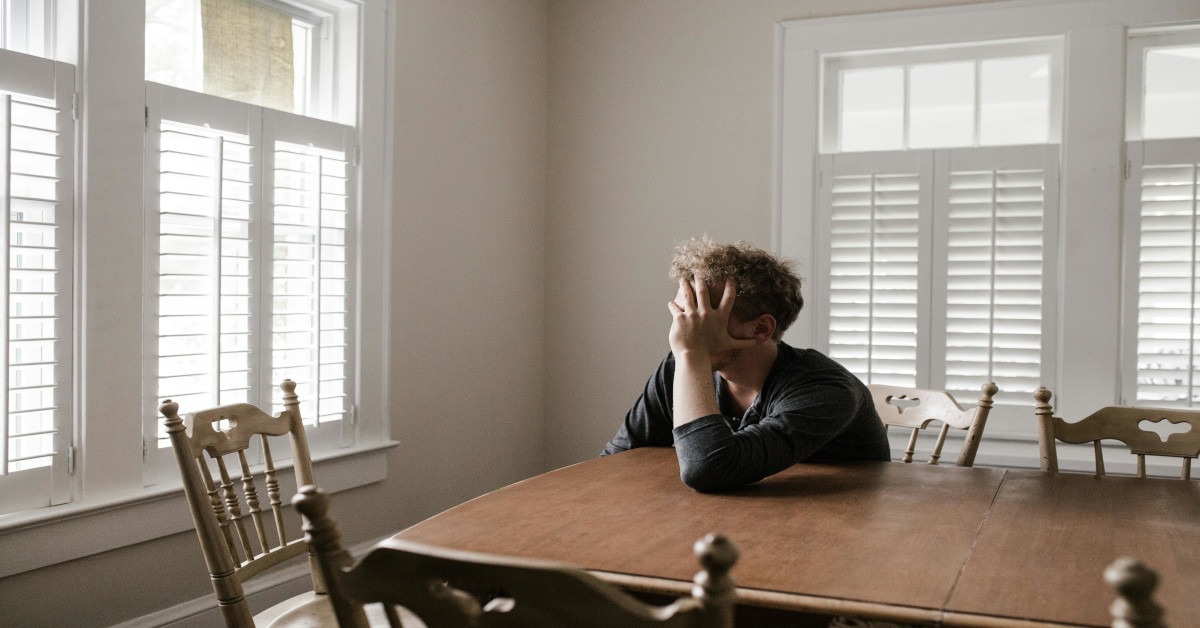 A depressed person holding his head while sitting at a table at home.