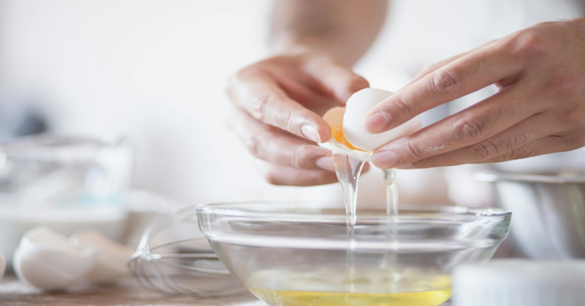 A person breaking eggs in a bowl.