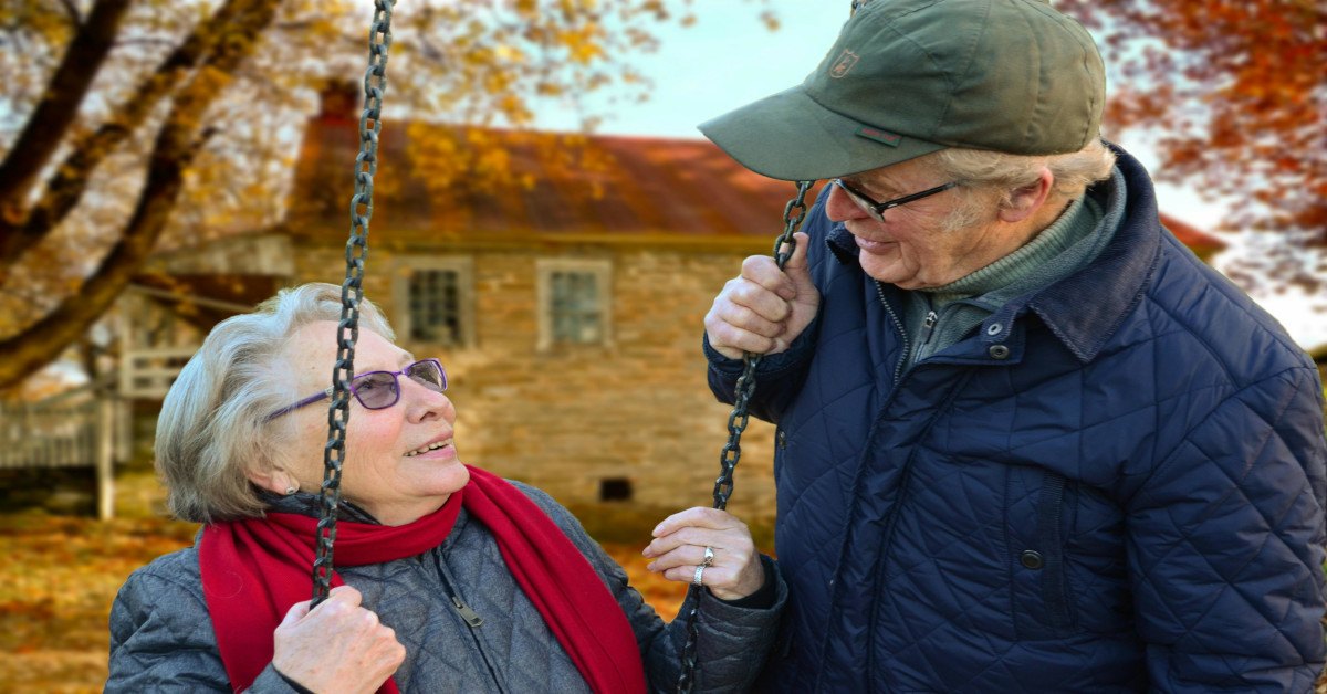 Image of an elderly couple smiling while looking at each other.