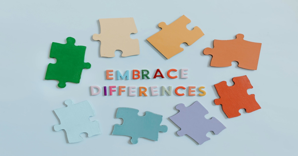 Different color puzzle pieces with the sentence "embrace differences" written in multiple colors in the middle of the puzzle pieces.