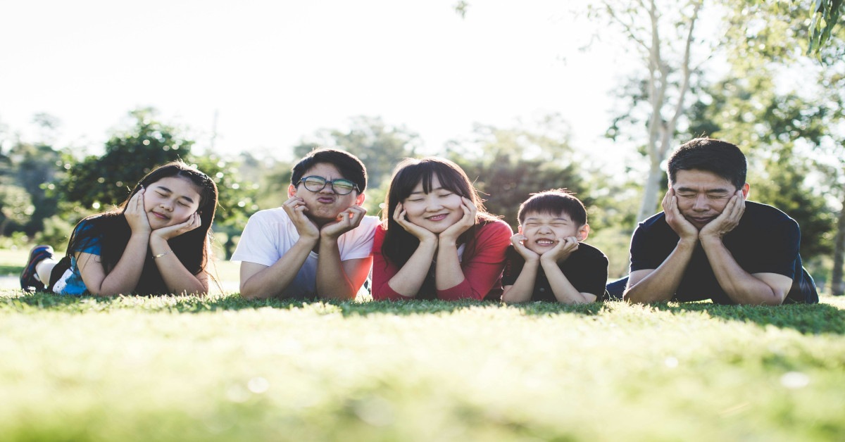 A family lying on their stomach while smiling for their camera and holding their face outside.