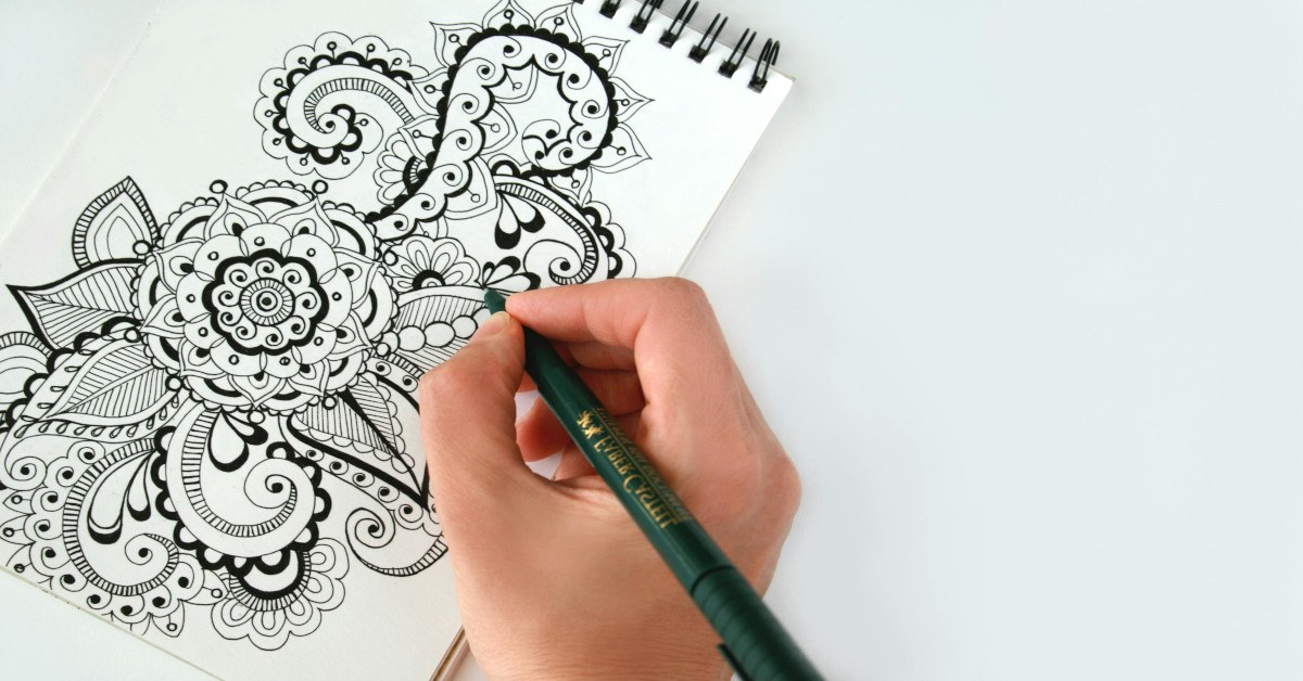 A person's hand holding a pen and sketching a black flower.