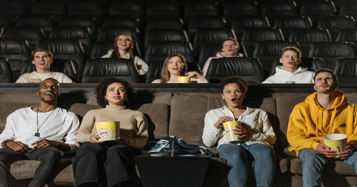 A group of friends is watching a movie together in a theater while eating popcorn.