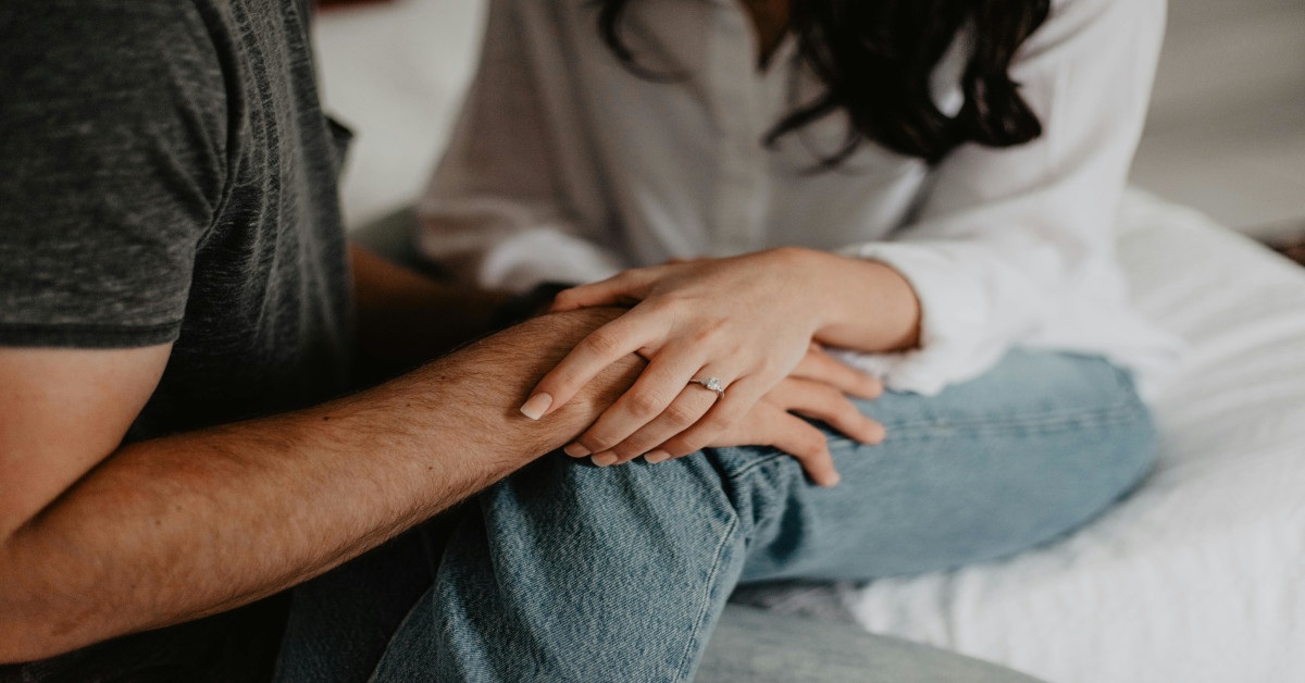A woman holding a man's hand on the couch.