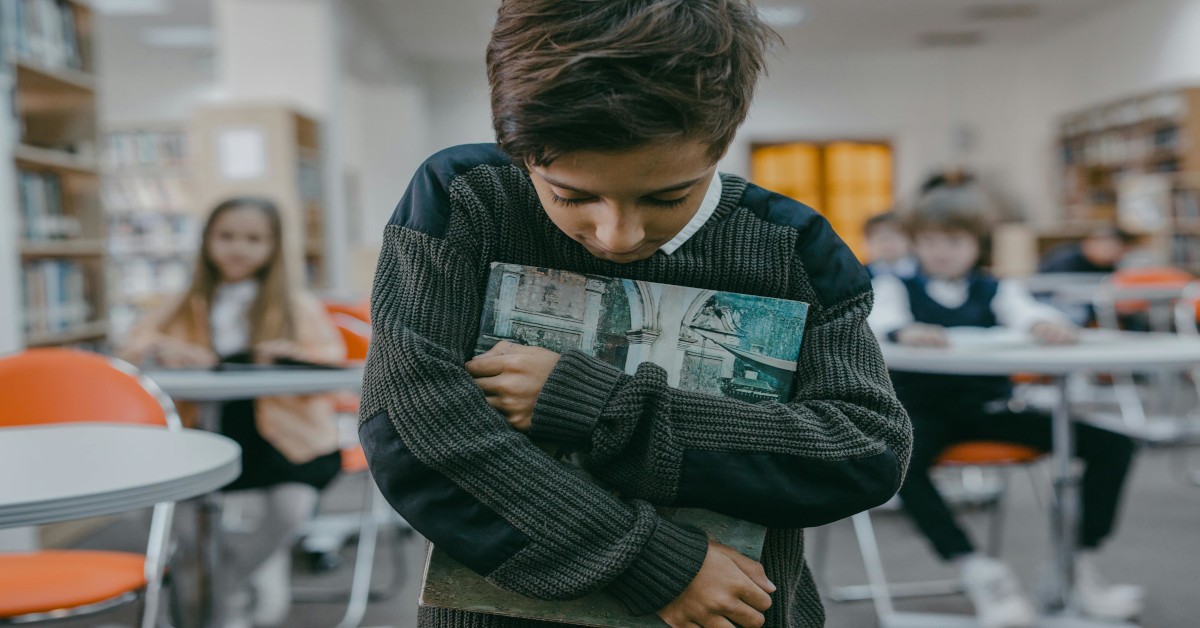 Image of a child looking down and walking away from his friends in a classroom.