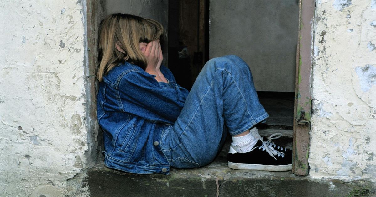 A lonely girl sitting in the doorway while holding her face, indicating she's sad.