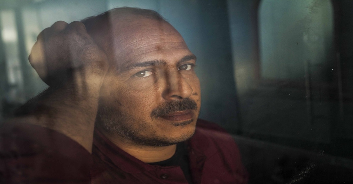 A lonely man holding his head and looking sad in front of a window.