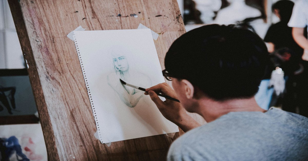 A man drawing a person's face on a canvas.