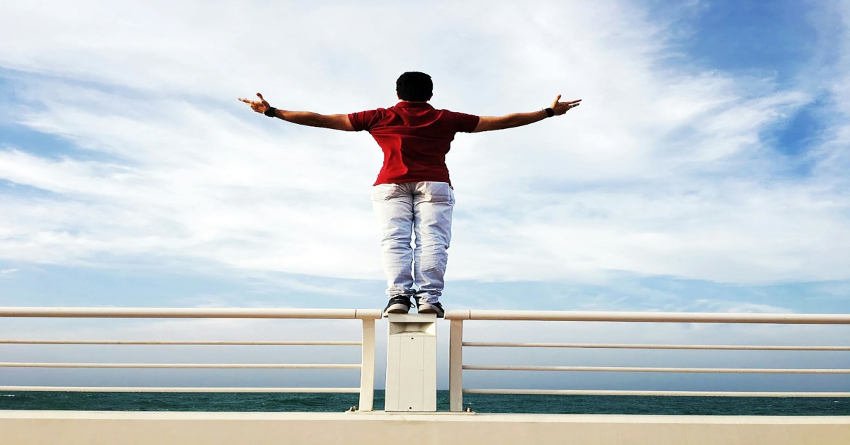 A man standing on a pier while holding his arms out indicating his freedom.