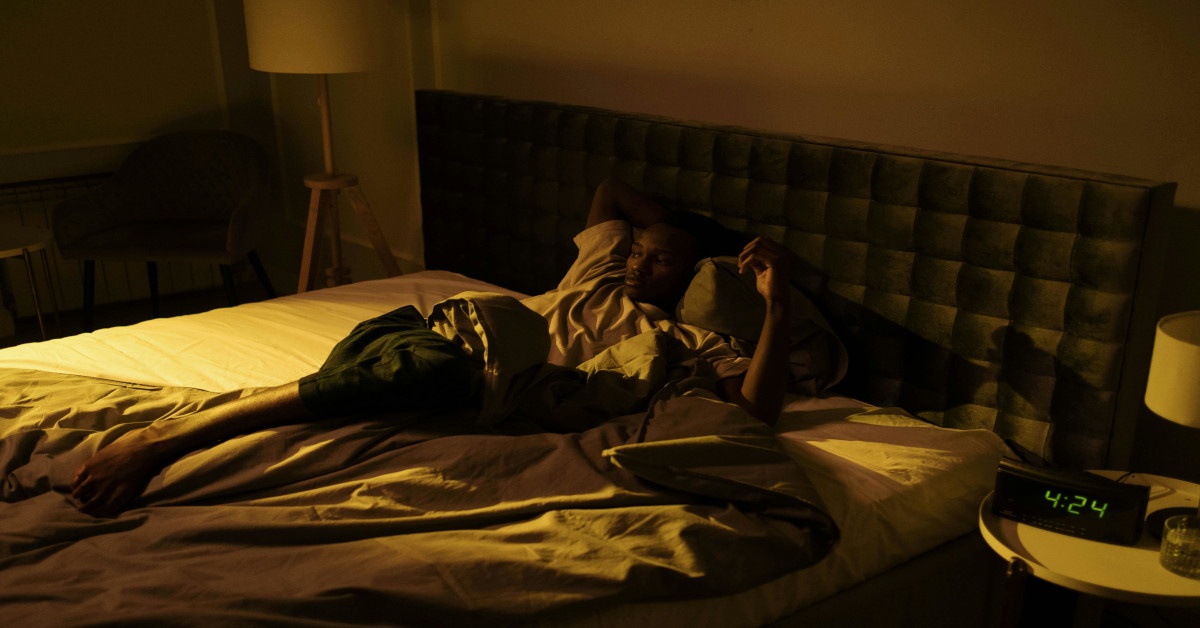 Image of a man lying awake in bed, unable to sleep, with the clock reading 4:24.