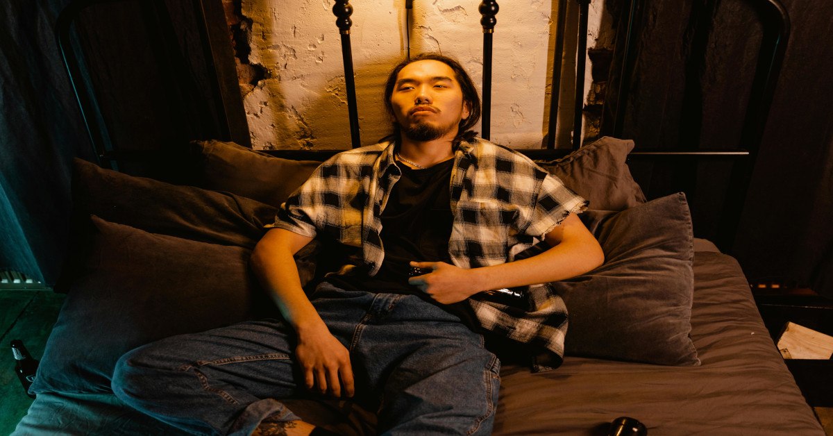 A man lying in bed with his clothes on while looking tired and unmotivated.