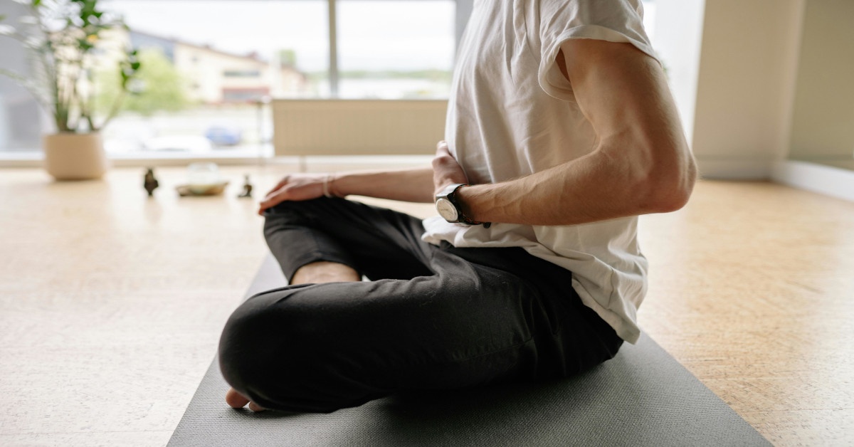 A man is sitting in a yoga pose while putting one hand on his belly.
