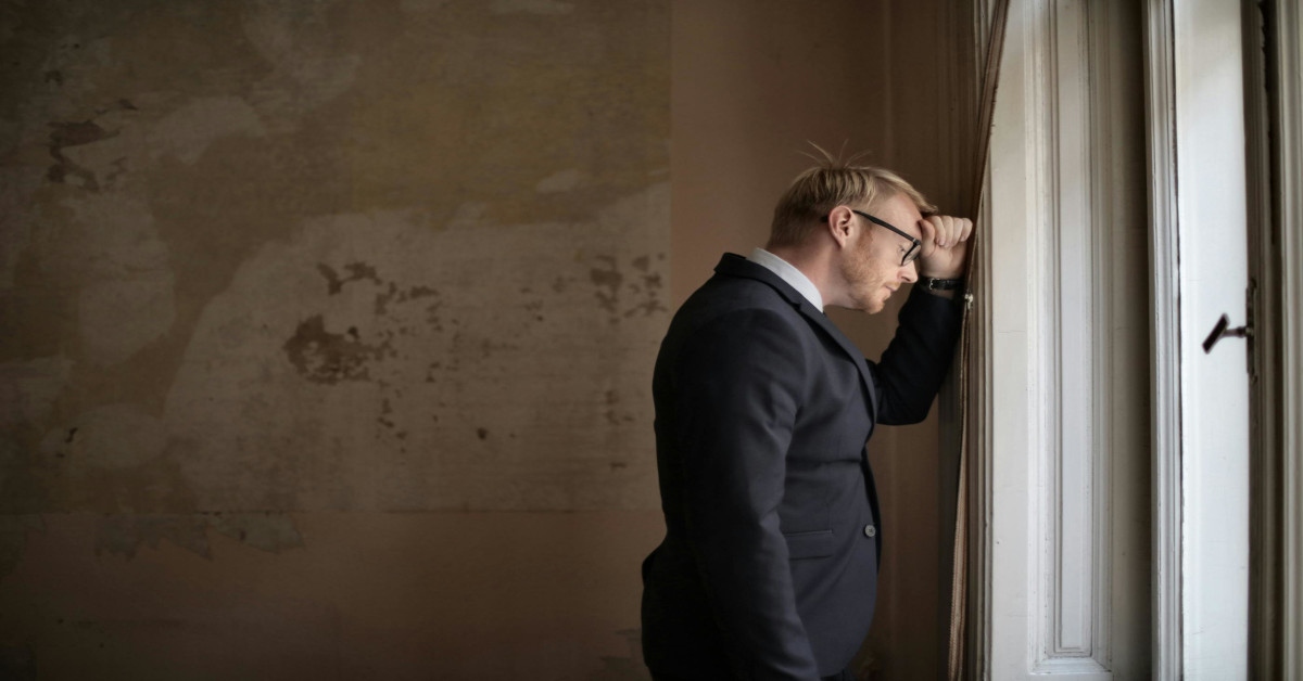 A man leaning against the wall with his head and hand while looking hopeless.