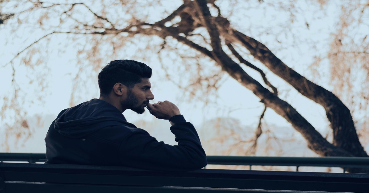 A man sitting outside on a bench while thinking.