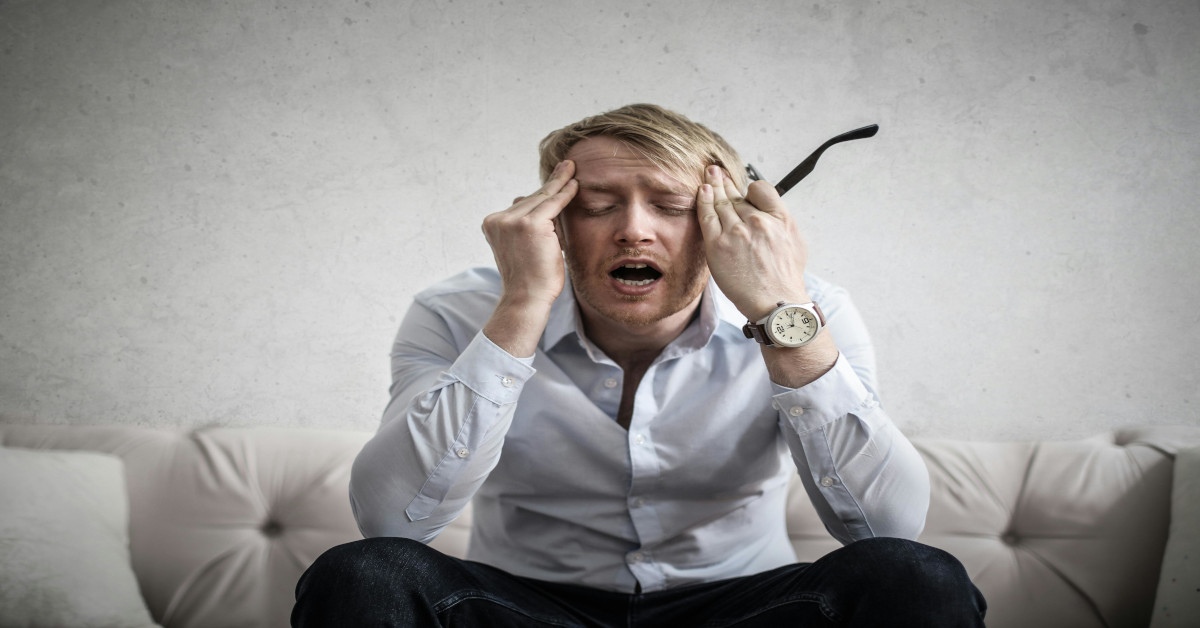 A man touching his head while holding his glasses with an open mouth.