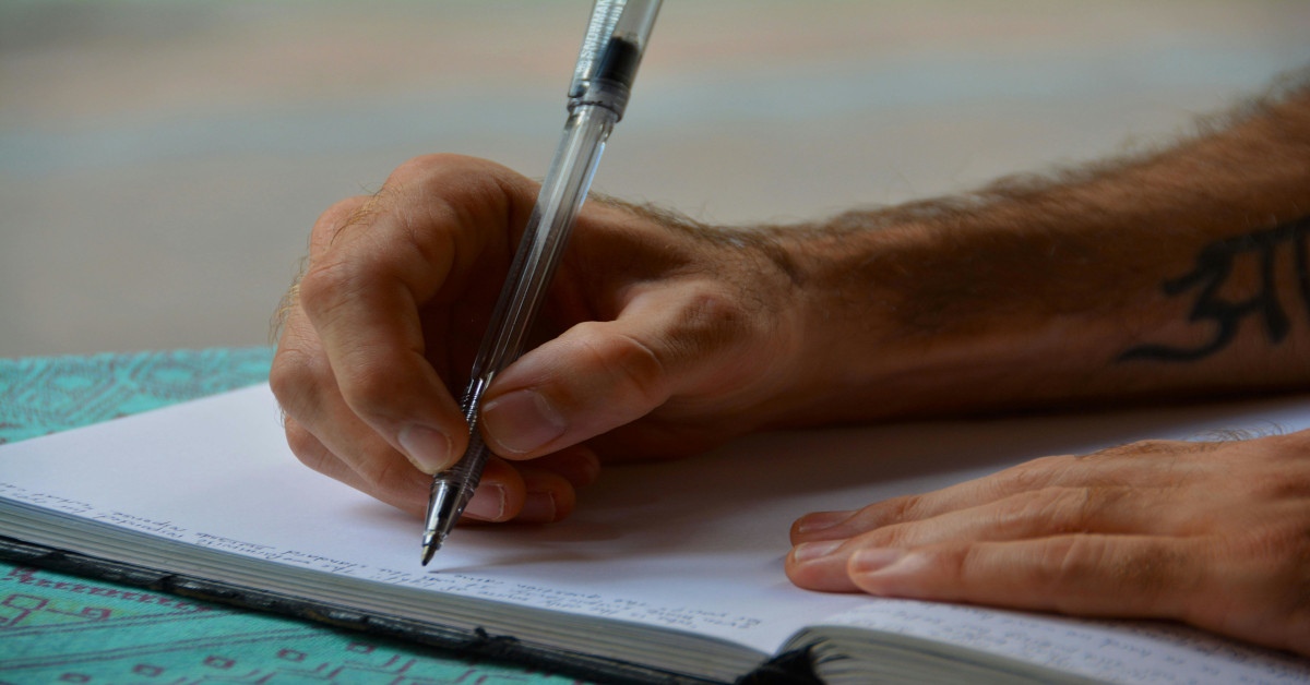 A man with a tattoo on his arm writing in a notebook.