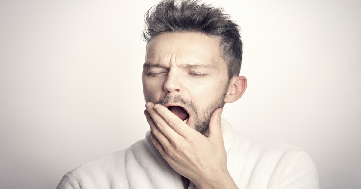 A man covering his mouth with his left hand while he's yawning.