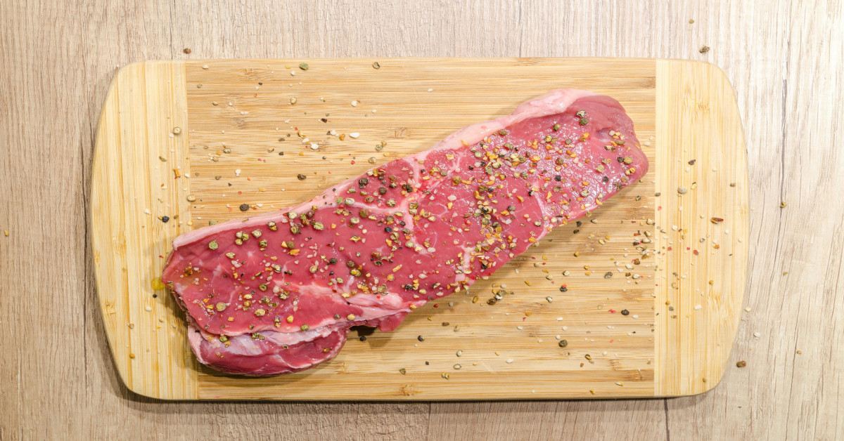Red meat is being seasoned while lying on a platter.