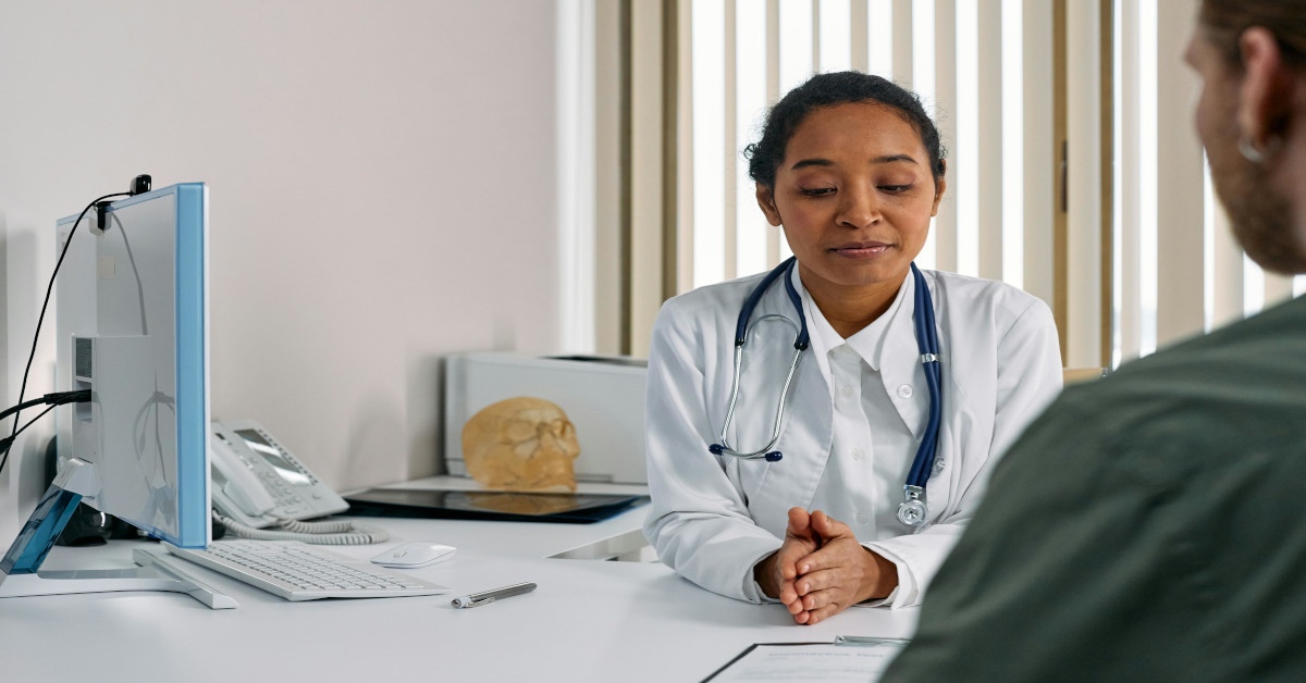 A man sitting at a medical appointment with a doctor explaining things.