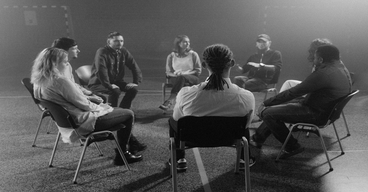 A black and white image of a peer support group sitting in a circle.