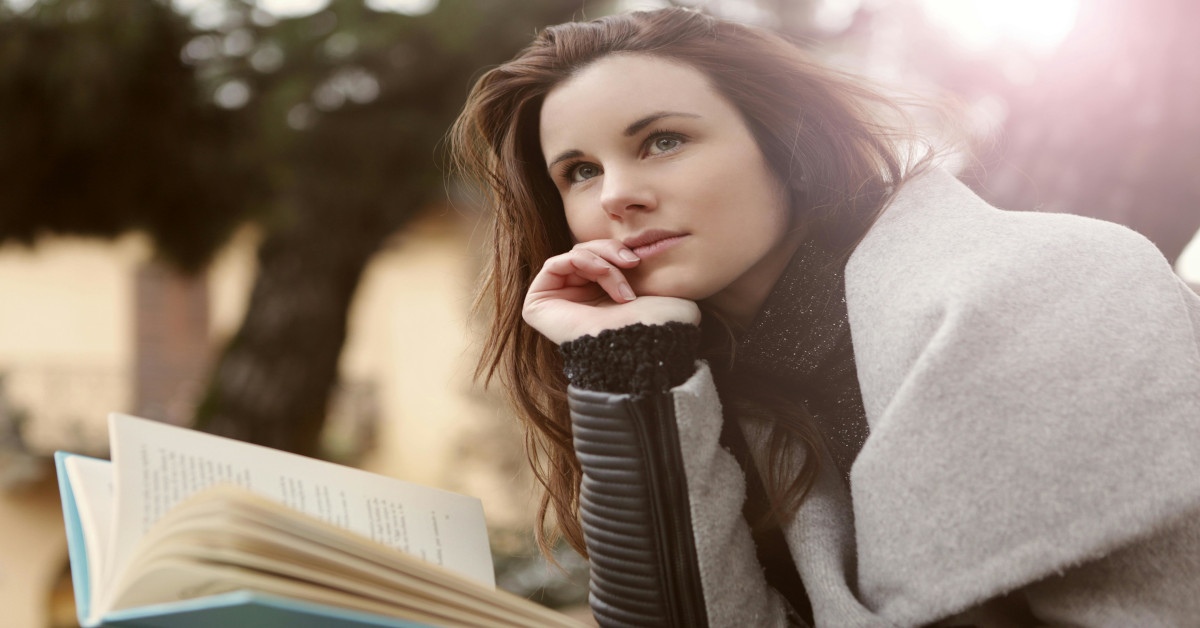 A pensive woman holding a book while thinking.