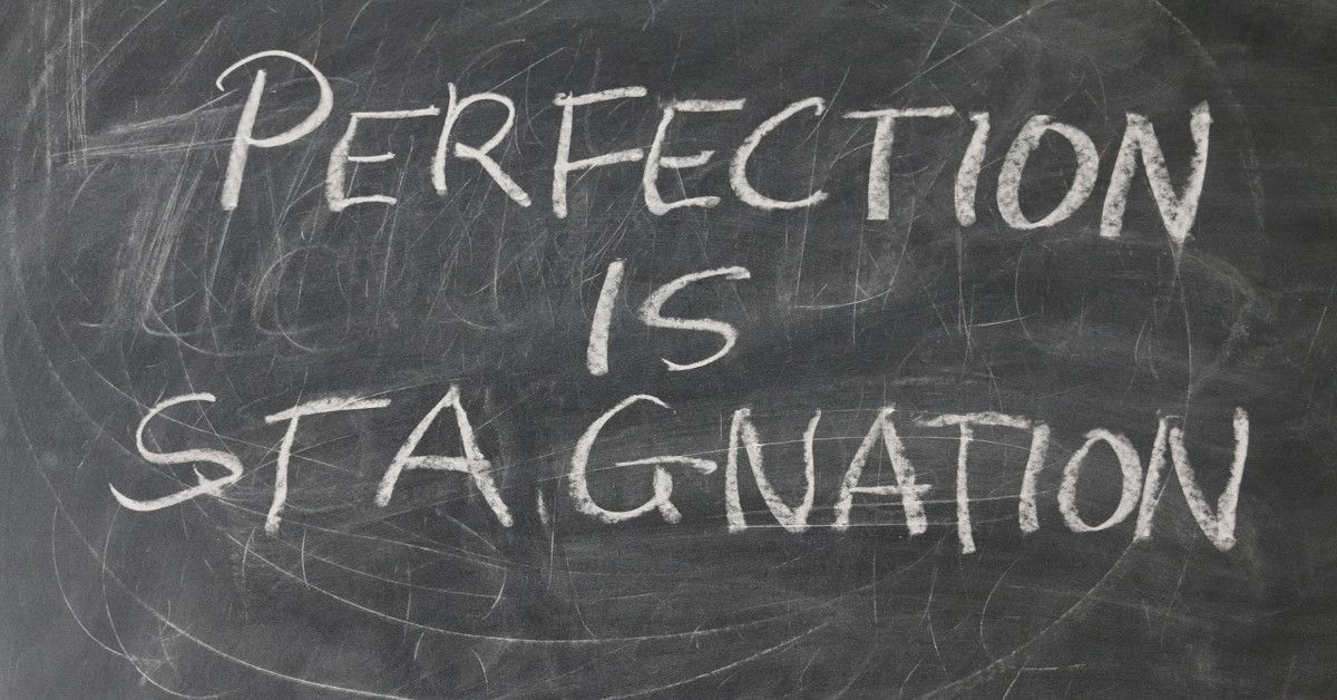 "Perfection is stagnation," written in white chalk on a blackboard.