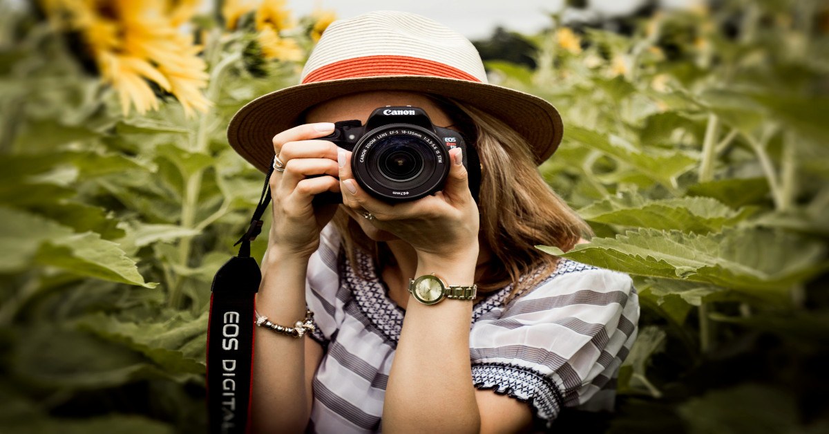 A woman photographing while looking at the camera.