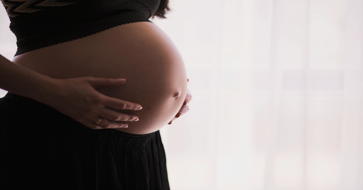 A pregnant woman holding her belly with both hands.