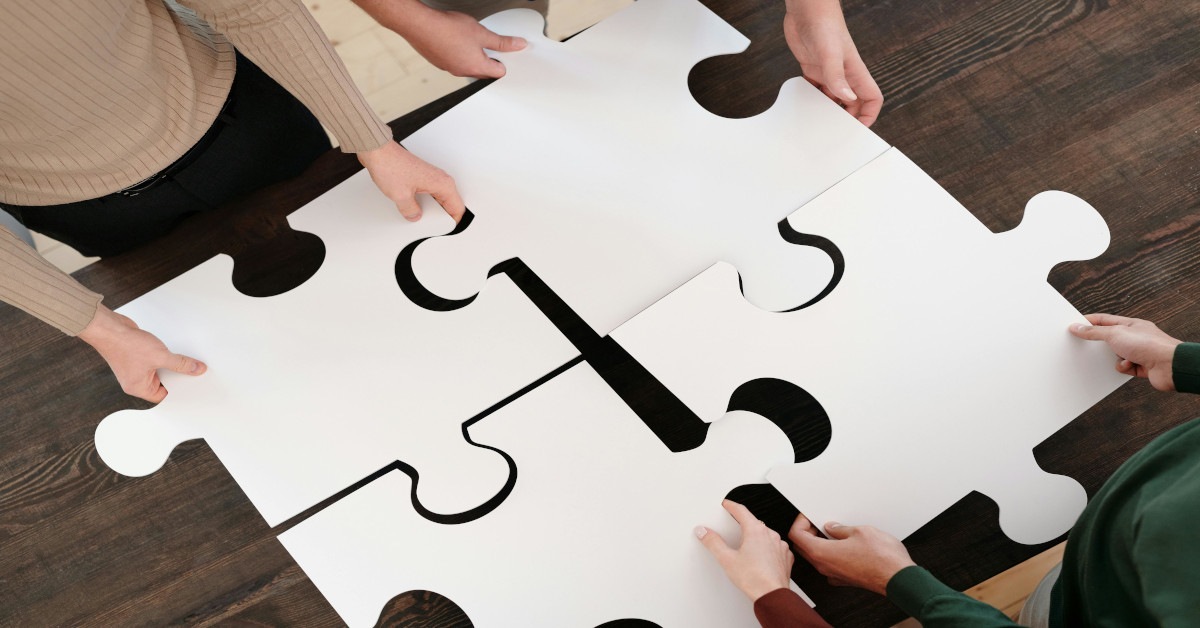 Multiple people fitting large puzzle pieces together on a table.