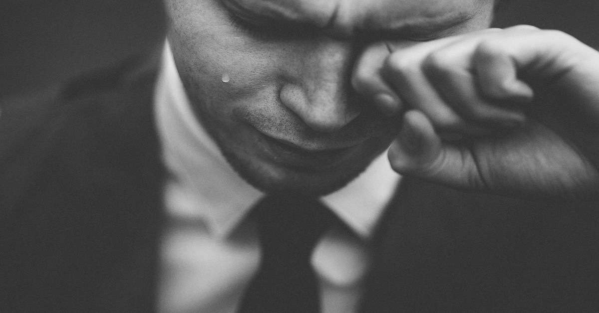 A sad man crying while wiping his eye.
