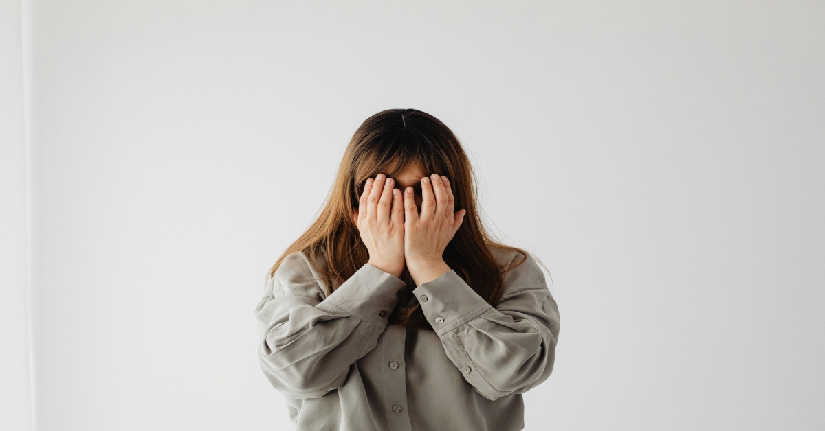A shy woman holding her hands in front of her face.