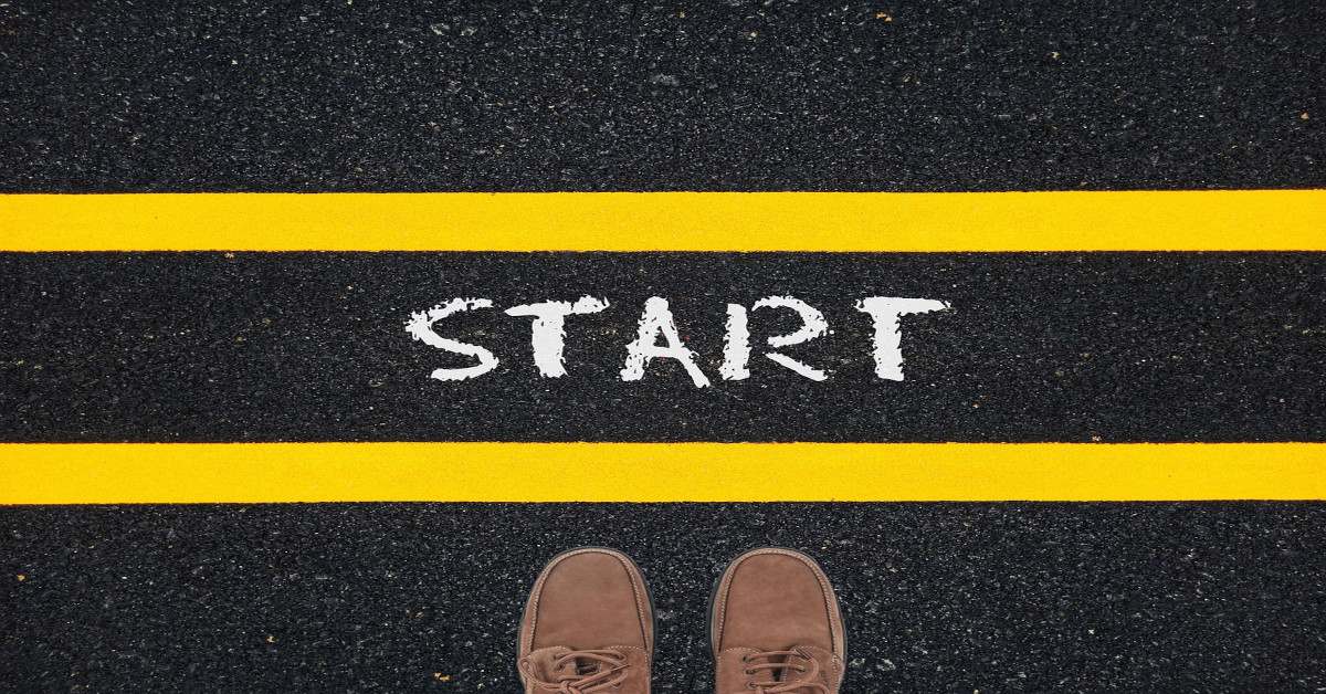 A man standing before two yellow lines with the word "start" written in white paint in the middle, indicating it's the starting line.