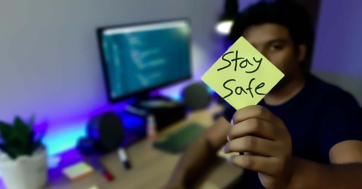 A man holding a yellow note reading, "stay safe".