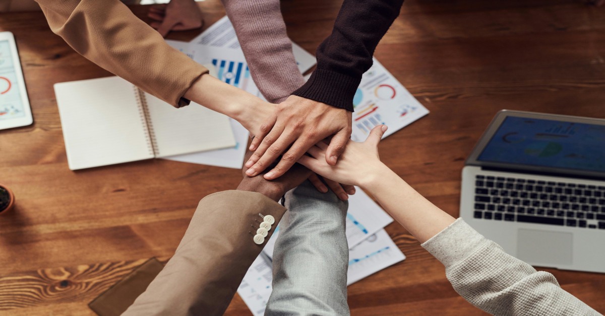 A group of colleagues putting their hands on top of each other, showing their support and teamwork.