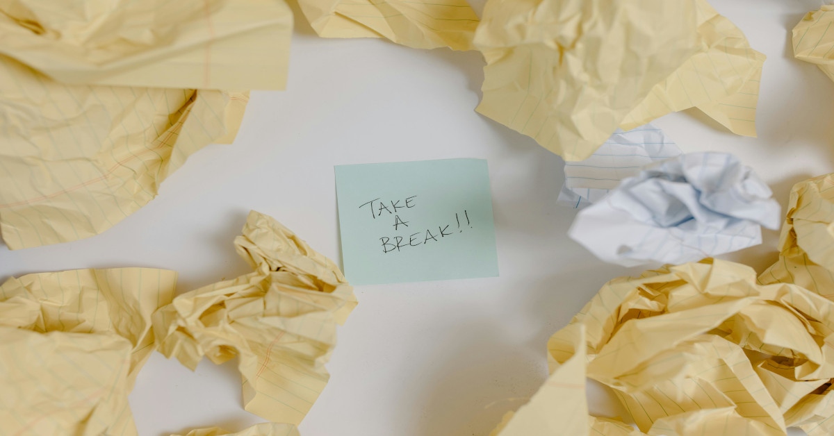 "Take a break" written on a post-it note that's lying on a table surrounded by crumpled pieces of paper.